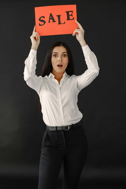 a woman in a dress shirt holding a orange sale sign