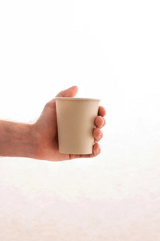 a hand holding a paper cup against a light background