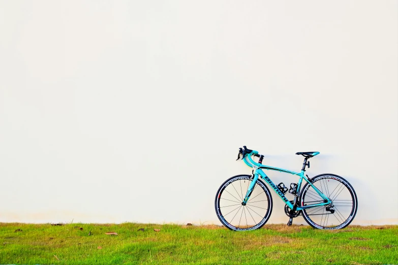 a bicycle parked against a white wall with grass