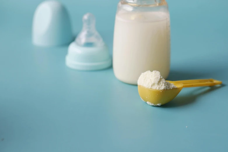 there are three small plastic spoons next to a bottle of milk