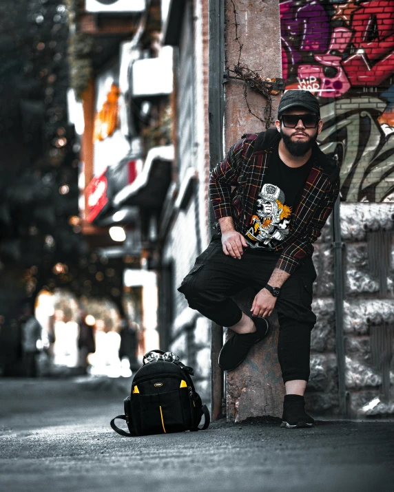 a young man wearing a backpack sitting next to a wall