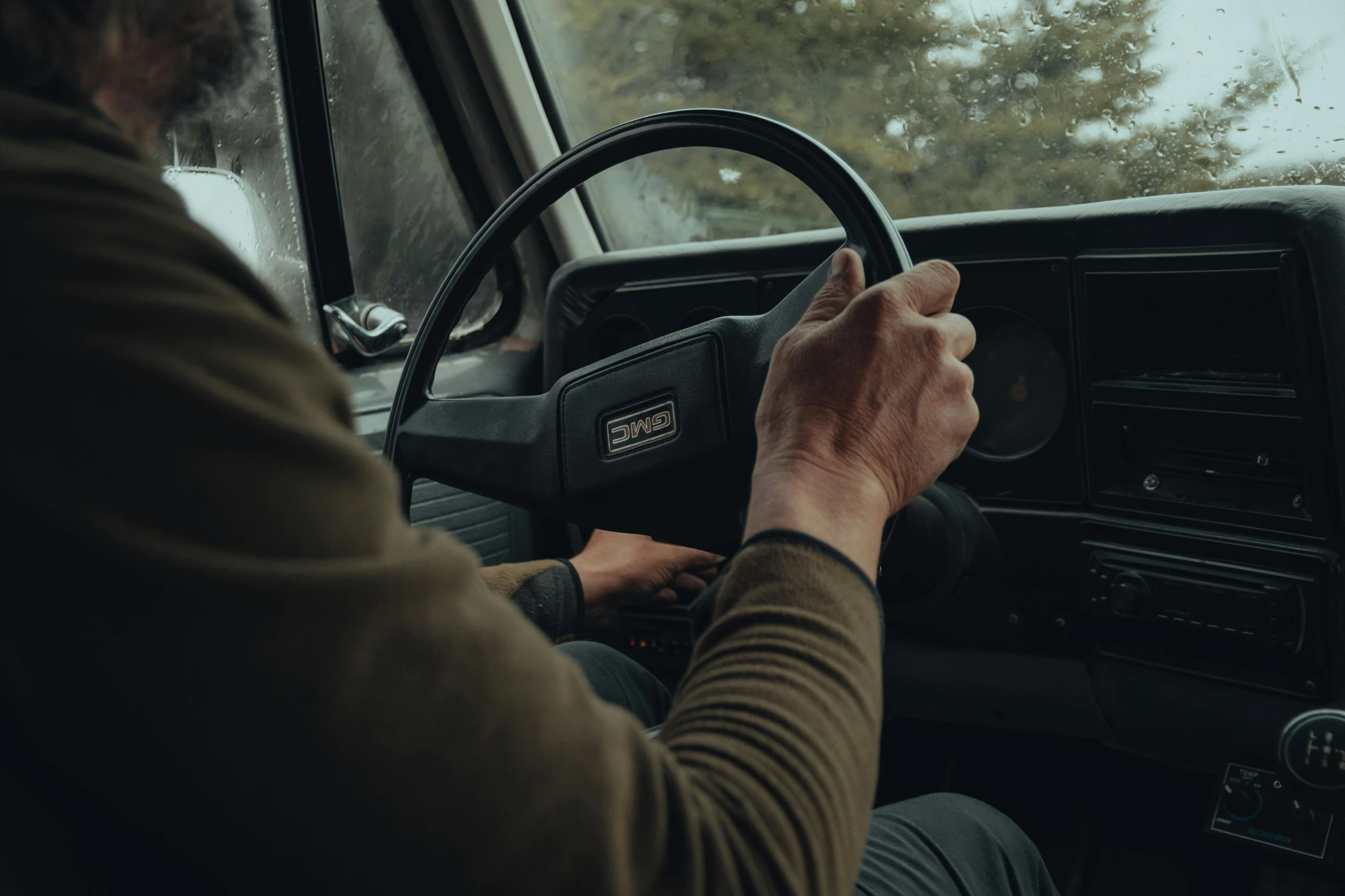 man driving his vehicle in the rain while holding a steering wheel