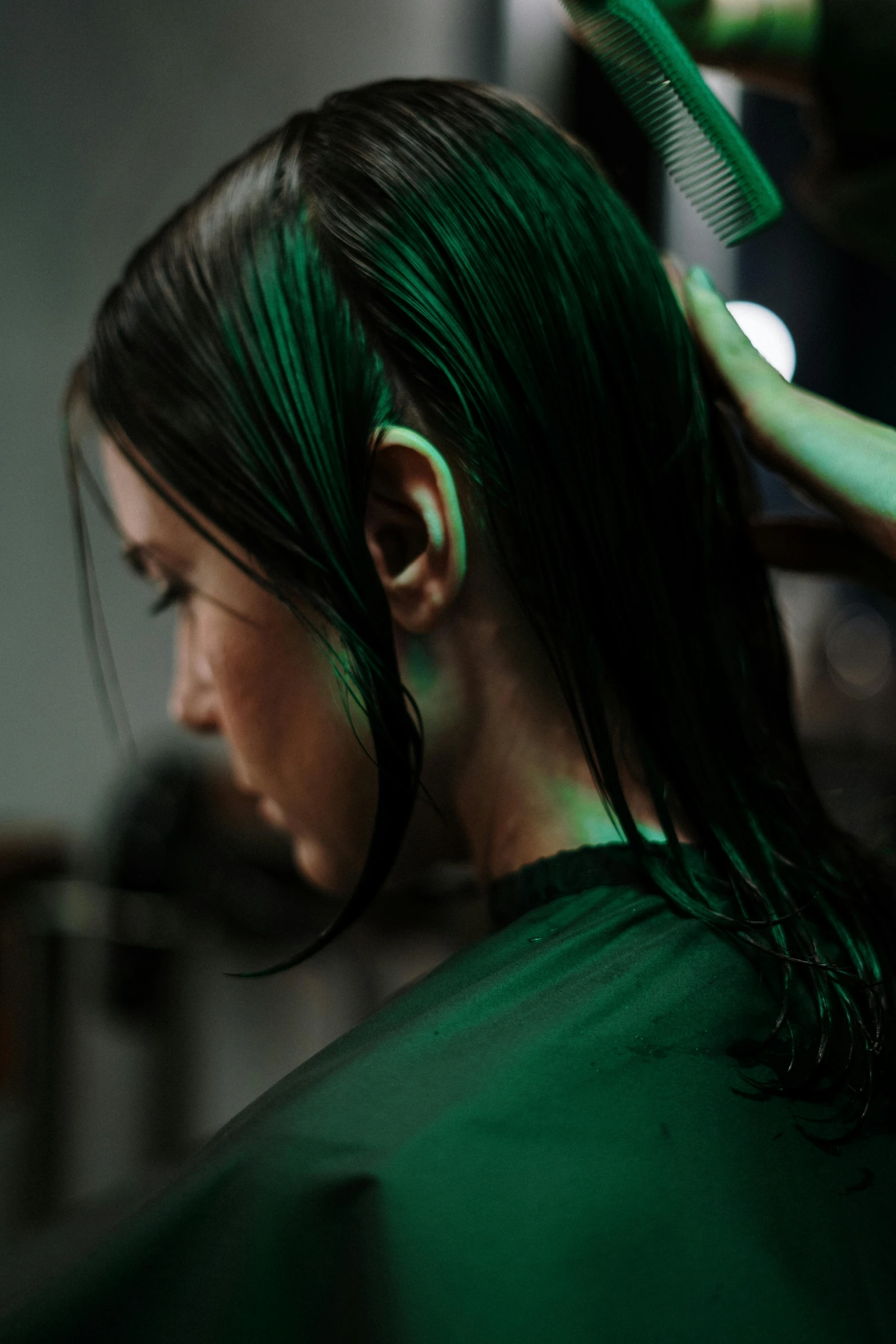a woman with dark green hair and neon green highlights is getting her hair dyed