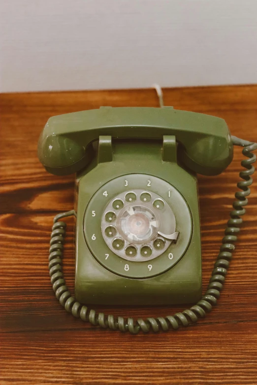 a green old fashioned telephone sitting on top of a wooden desk