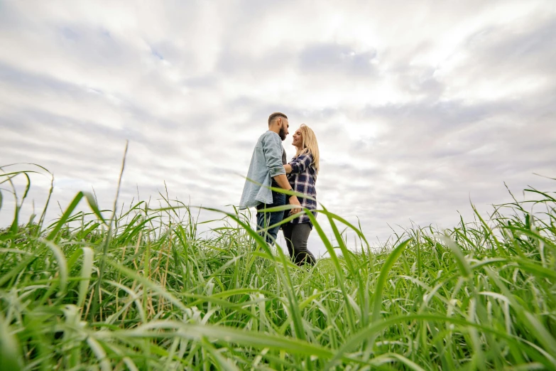 an engaged couple stand in tall grass together