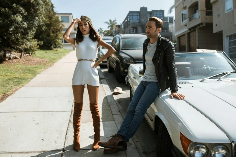 a young couple standing on the street next to a parked car