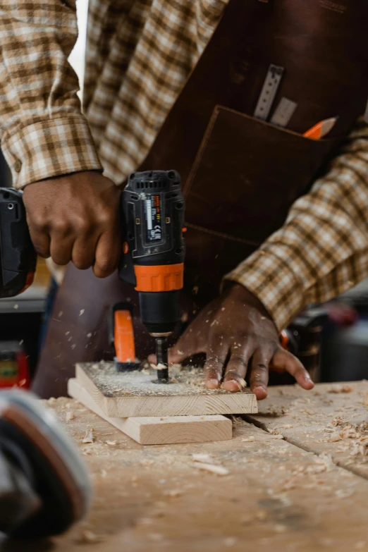 a person holding a drill gun while  a piece of wood