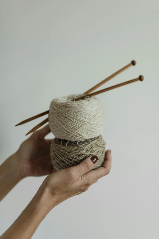 hands hold twined needles and skeins of yarn