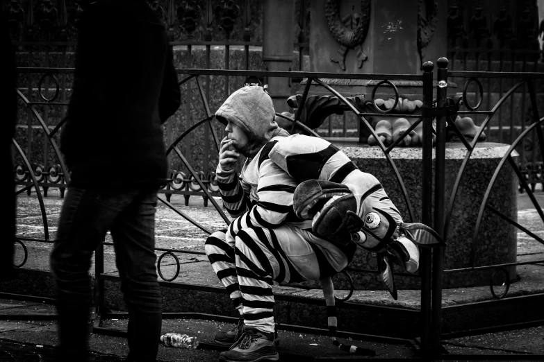 man in striped jacket sitting on wrought iron fence