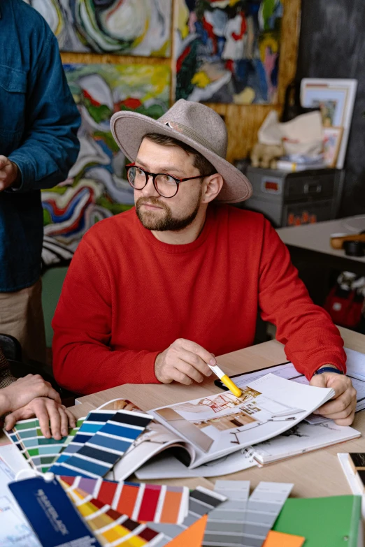 the man in red shirt and hat is sitting at the table with some color samples