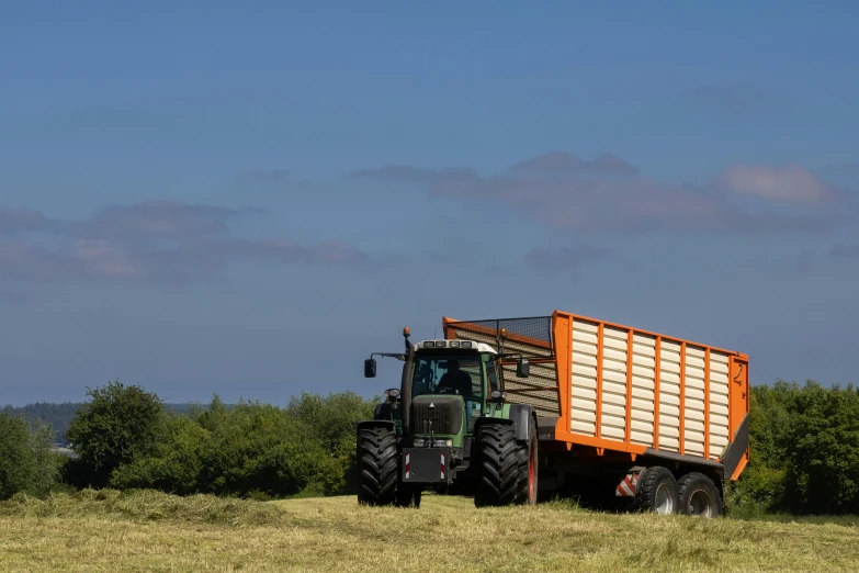 a tractor pulls a trailer behind it through a grassy field