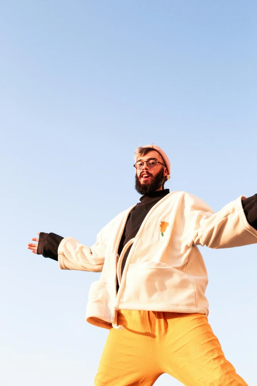 a man is posing with his arms extended, against a blue sky