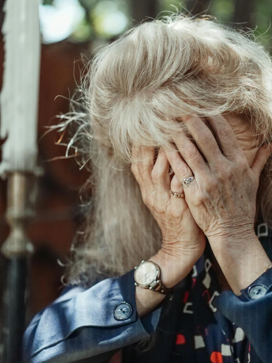 an old woman covering her eyes while standing in front of a wall