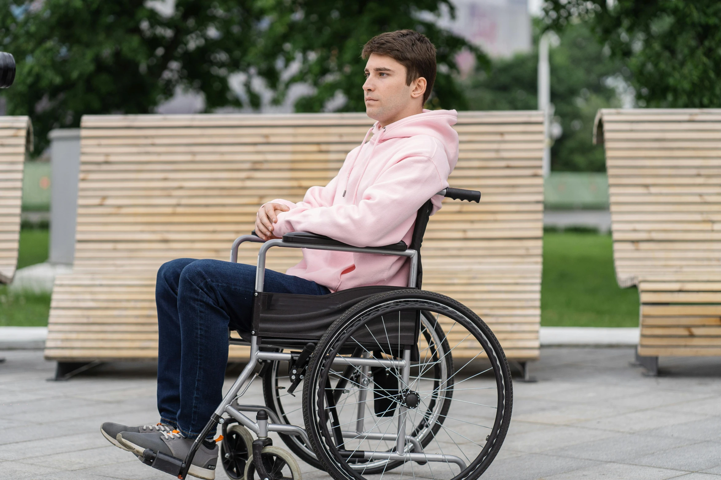 a young man in a wheelchair sits near several park benches