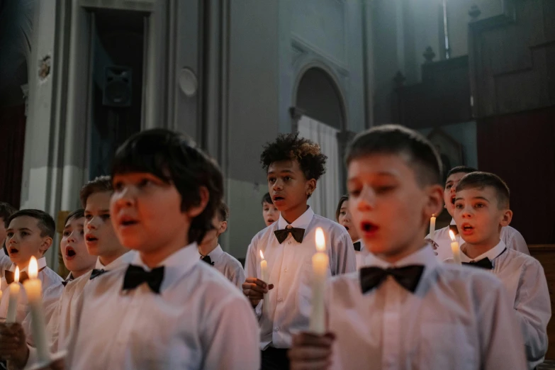 s wearing ties and bow ties singing in front of a church with candles