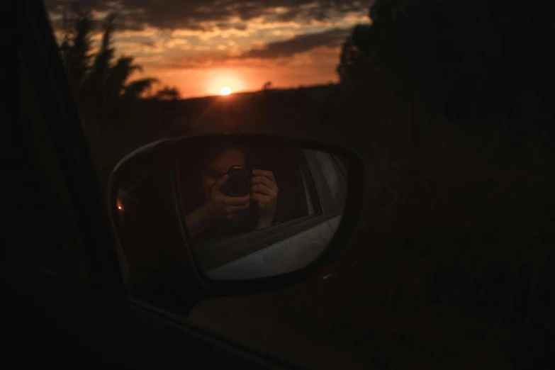 a car's rear view mirror reflecting the setting sun