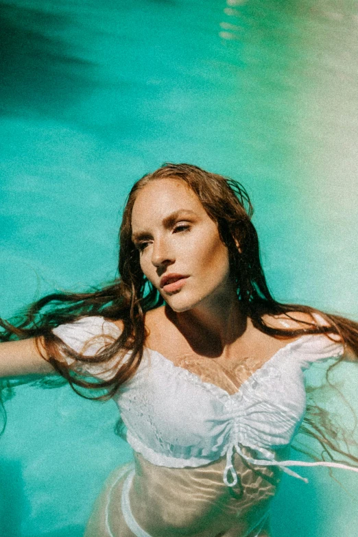 an attractive woman wearing a white top and holding her hair in the ocean