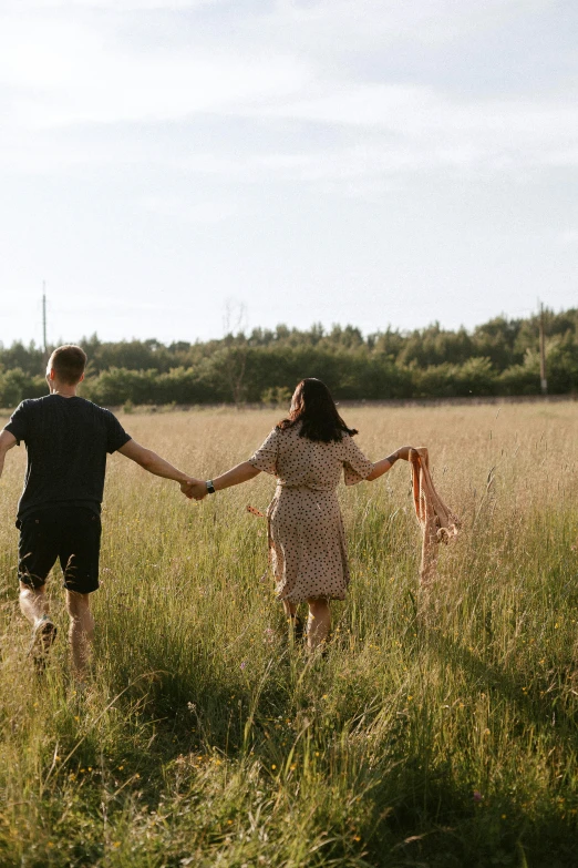 man and woman hold hands in a field of tall grass