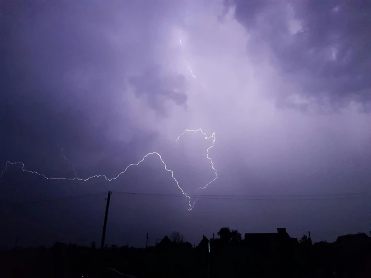 a lightning is seen over houses and trees during a storm