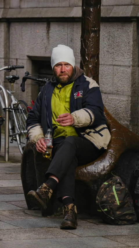 the man sits outside of the statue drinking beer