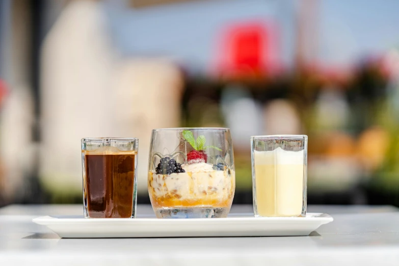 three glasses of liquid and some fruit on a plate