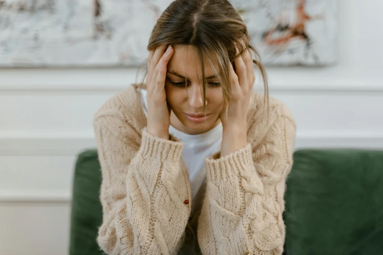 woman sits on a green chair, with one hand up to her head