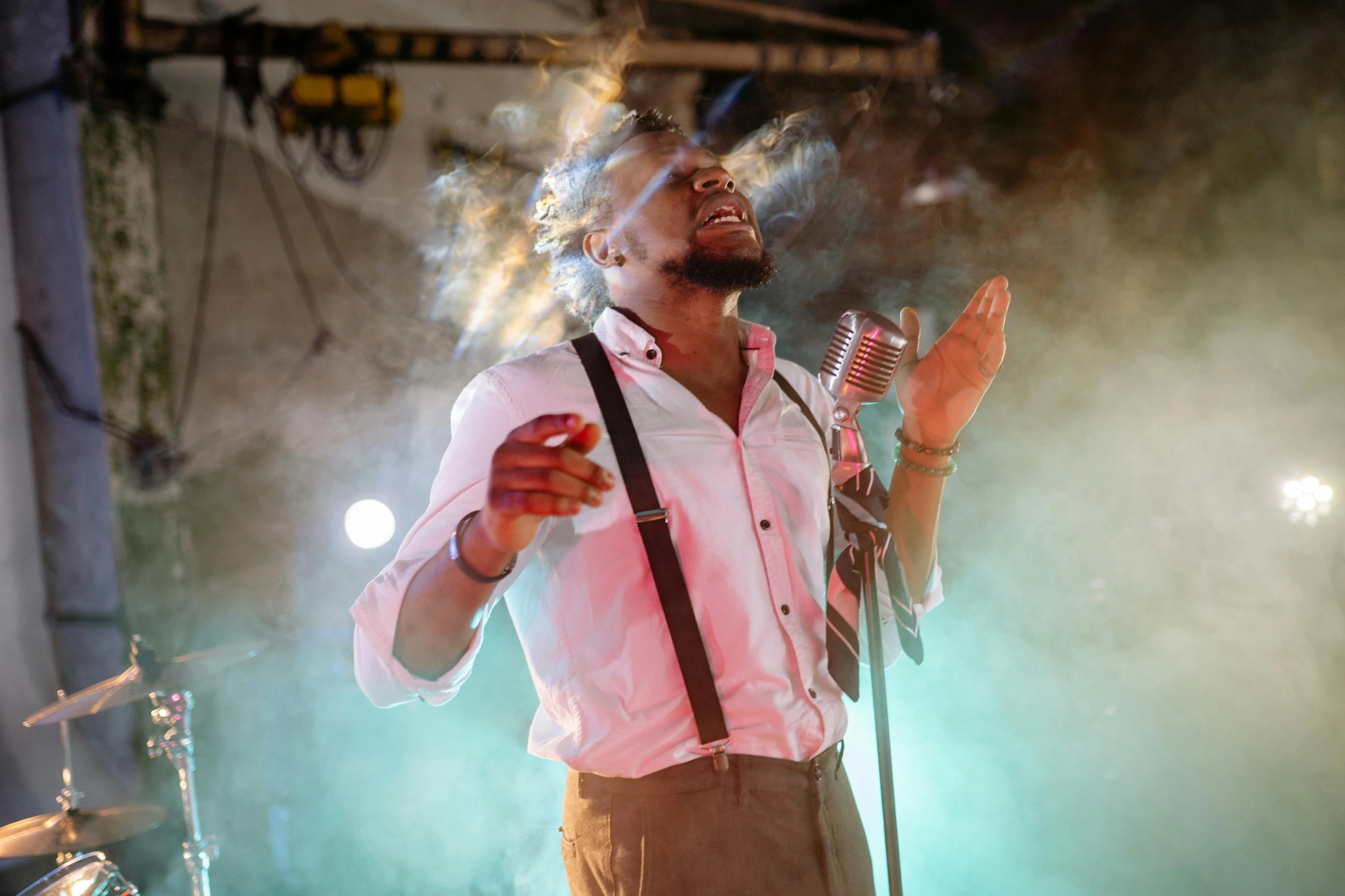 a young man in overalls sings on stage