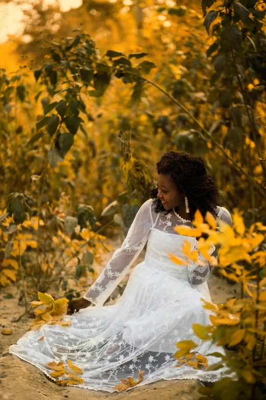 a lady in a lace gown is sitting on a field with yellow flowers