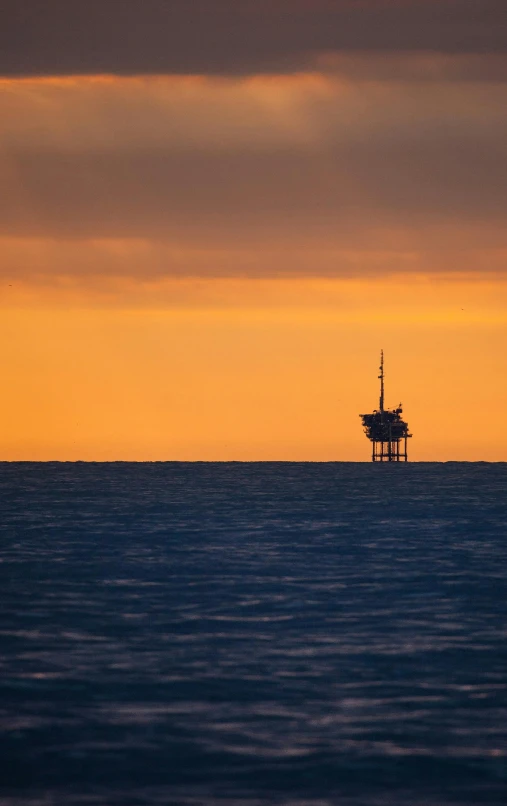 there is an oil rig on the water at dusk