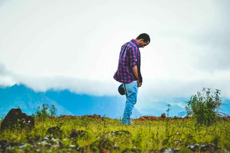 a man in plaid shirt standing on grassy field with mountains in the background