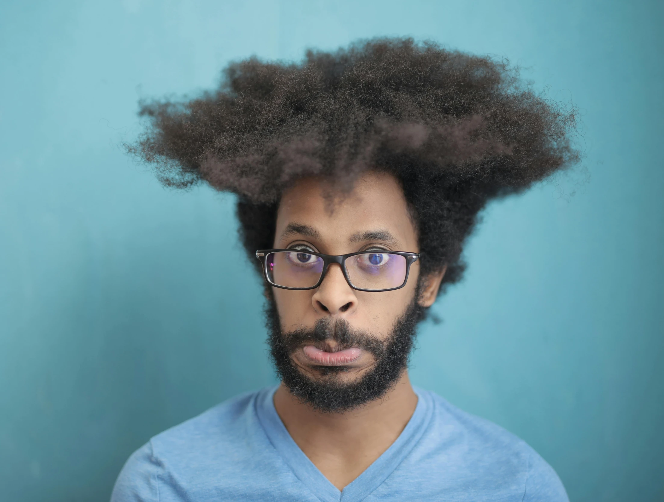 a man with curly hair and glasses making a funny face