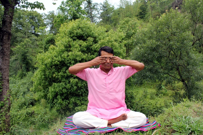 a man in pink shirt and white pants sitting in grass