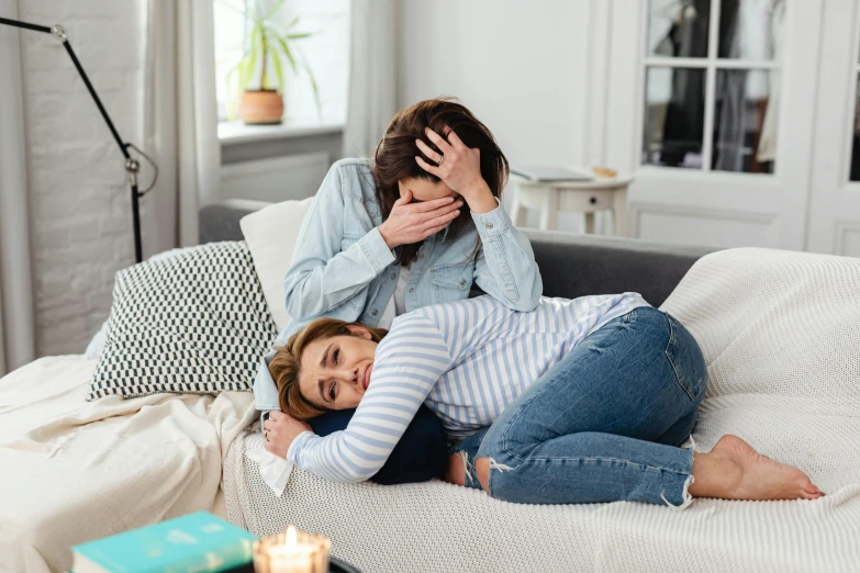 two women cuddle on a bed one holding her head