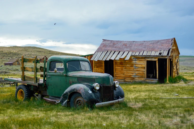 an old, old green truck is parked in front of a rundown barn