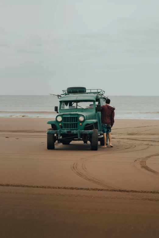 a person in a green truck sitting at the ocean's edge