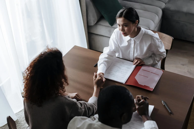 two woman sitting at a table discussing soing with a man on the other side of the table