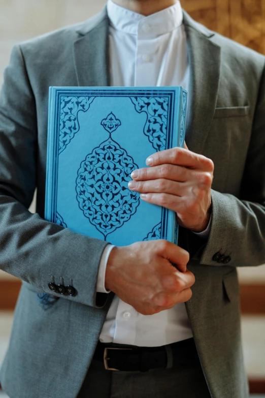 a man is holding up a book with islamic writing on it