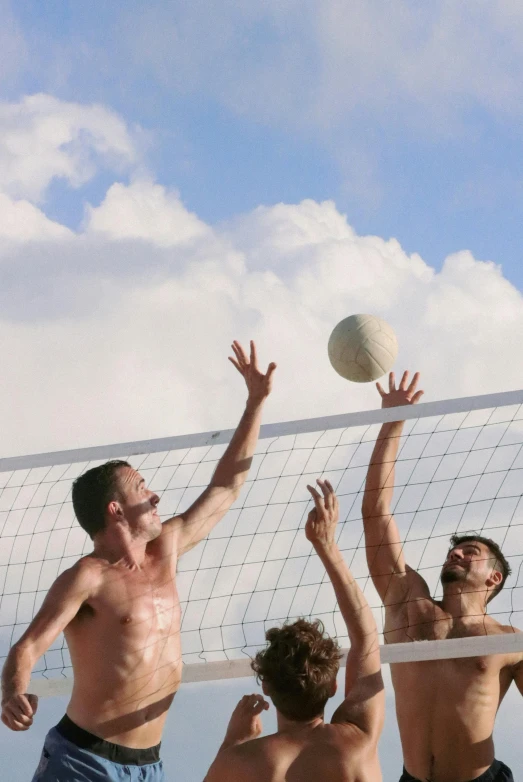 four shirtless men playing volleyball on the beach