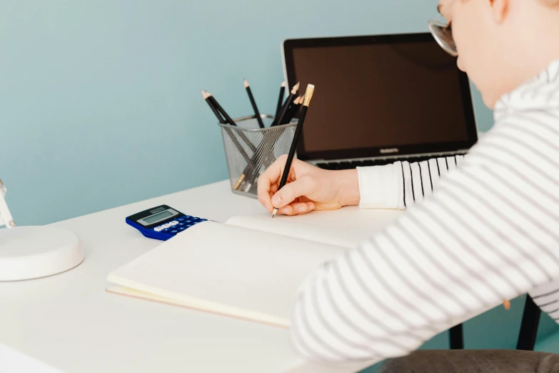 a person using their lap top with a pen and pencil