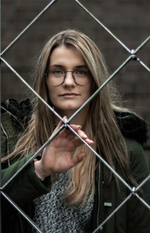 woman standing behind a chain link fence in front of a wall