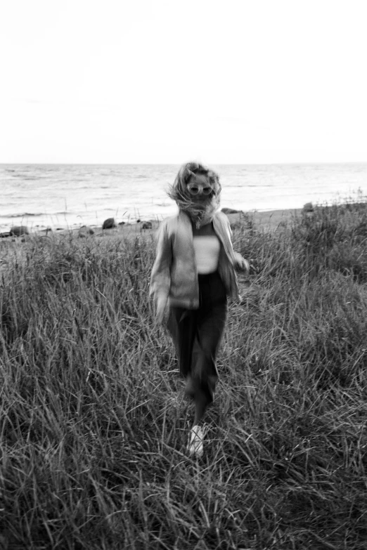 a woman walking through a grass field next to the ocean