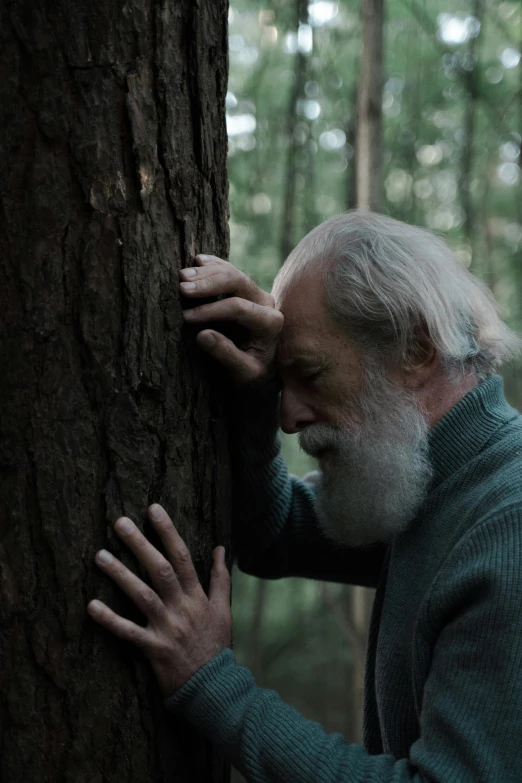 an older man in the woods holding onto a tree
