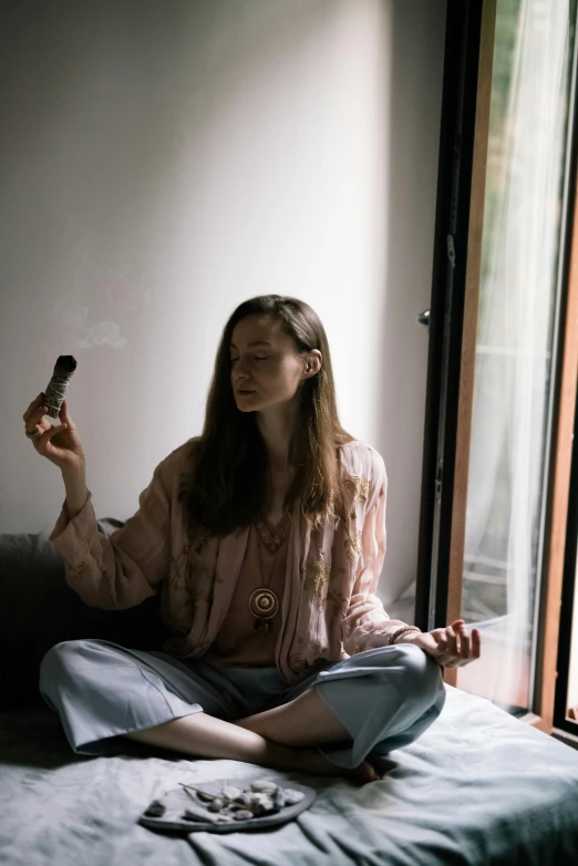 woman in white jacket sitting on a bed holding up a phone