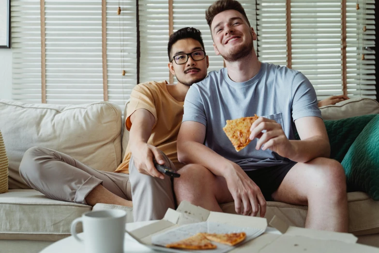 a couple of people sitting on a couch and holding pizza