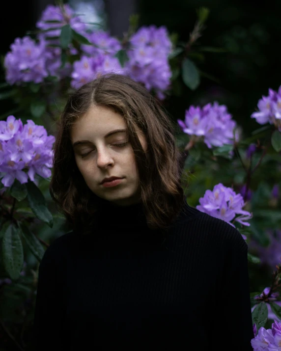 a woman wearing a black turtle neck top next to purple flowers