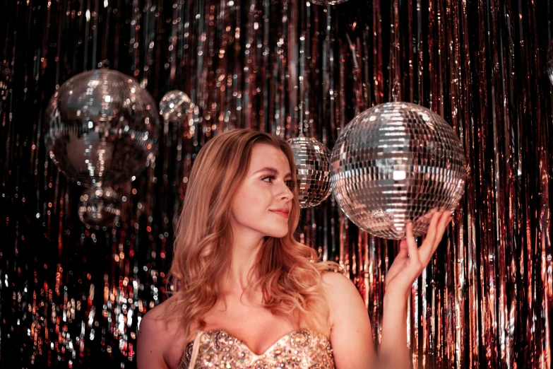 a blonde woman in a gold strapless dress holding onto two disco balls