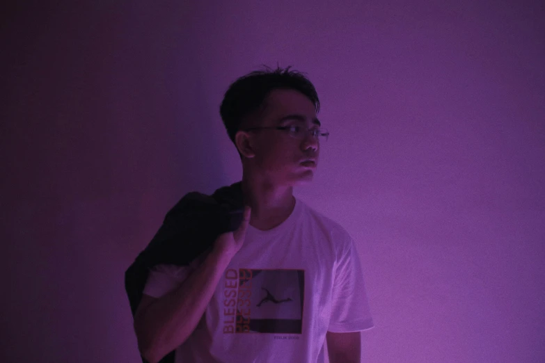 a man in the darkness standing against a purple lit wall