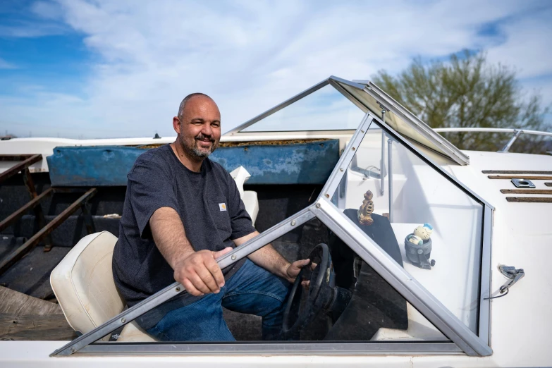 a man in a blue shirt smiling at the camera while sitting on a boat