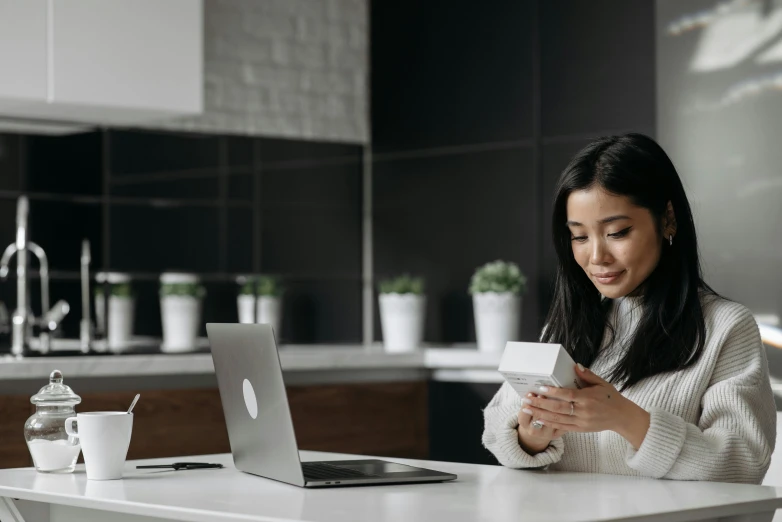 a woman using a cell phone sitting in front of her laptop computer