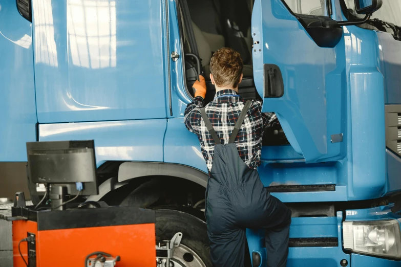 a man wearing overalls looking at the door to his semi truck